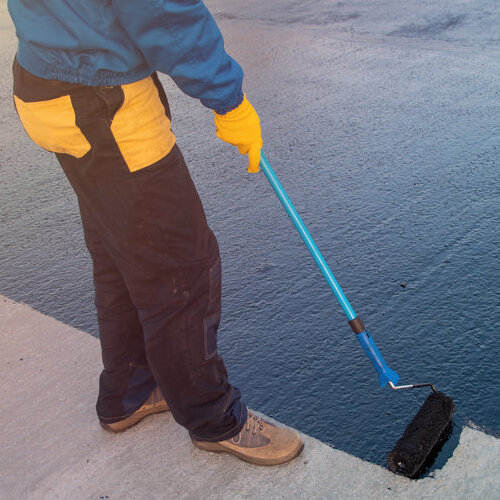 Roofer worker painting black coal tar or bitumen at concrete surface by the roller brush, A waterproofing. industrial worker on construction site laying sealant for waterproofing cement